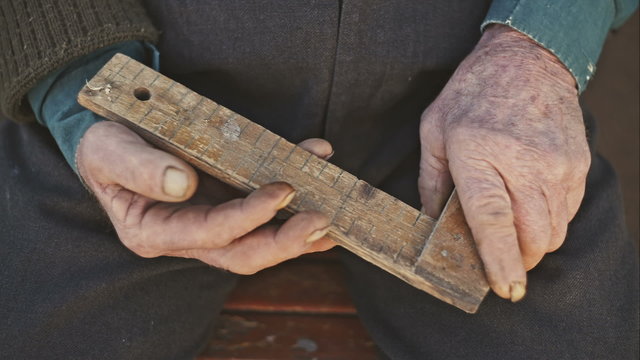 Hands of an old man holding a wooden angle and indicate the scale