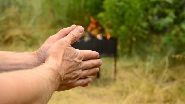 Hands of man with fire in brazier on background
