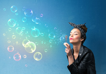 Pretty lady blowing colorful bubbles on blue background