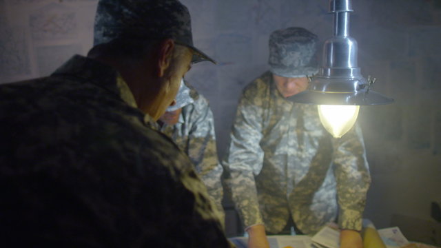  Military officers in army bunker, looking at map & discussing battle strategy