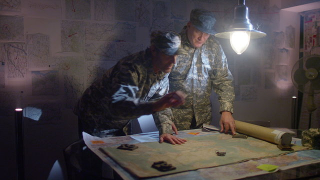  Military officers in army bunker, looking at map & discussing battle strategy