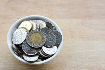 Concept of saving money, putting coins in a cup on a wooden floor.