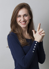 seduction concept - thrilled young woman making a hand gun sign with her fingers for sexy business fight, studio background