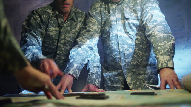  Military officers in army bunker, looking at map & discussing battle strategy