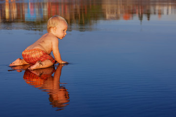 On sunset beach funny baby boy crawling on black wet sand to sea surf for swimming in waves. Family travel lifestyle, and water outdoor activity on summer vacation with child on tropical Bali island