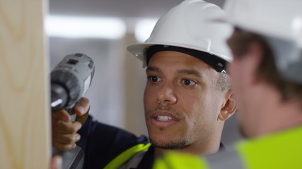  Male construction worker or tradesman working with male apprentice, showing him how to use a drill. 