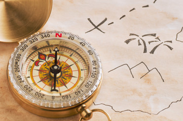 Fototapeta na wymiar Closeup of compass over stained yellowed paper sheet with part of hand drawn treasure map