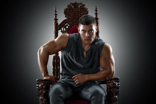Muscular young man in a T-shirt and jeans, sitting on the throne.