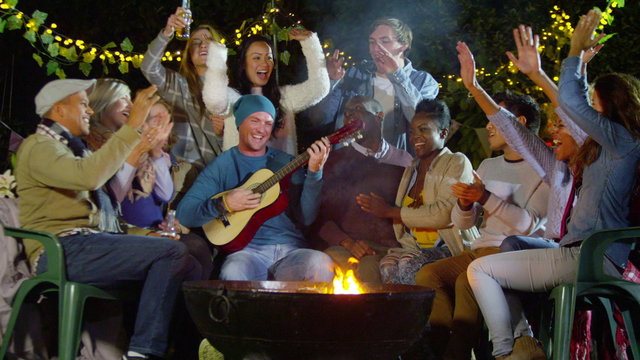 Happy mixed ethnicity friends socializing and playing guitar outdoors