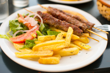 Souvlaki or kebab on skewers with potatoes and vegetables.