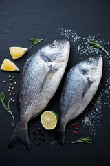 Two fresh dorada fishes on a black wooden background, above view