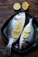 Two uncooked dorado fishes with salt, lemon and lime, above view