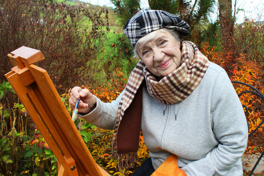 happy senior woman painting picture on nature