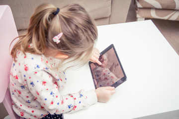 Little girl sitting at her pink chair with digital Tablet