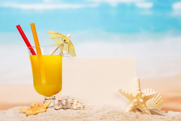 Fototapeta na wymiar White card on sandy beach and glass of cocktail