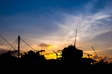 Industrial construction cranes and building silhouettes over sun