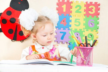 Cute child girl drawing with colorful pencils and felt-tip pen in preschool at table in kindergarten