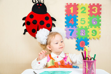 Cute child girl drawing with colorful pencils and felt-tip pen in preschool at table in kindergarten