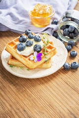 Belgian golden waffles for breakfast with fresh berries and flower honey on wooden background. The concept of home-cooked breakfast.