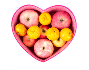 orange and apple mixed in heart-shaped gift box on white