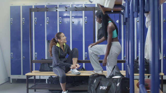  Cheerful attractive young women chatting in ladies' locker room at the gym