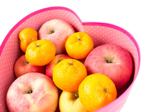 orange and apple mixed in heart-shaped gift box on white