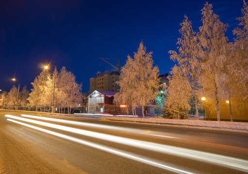 Winter skyline at night with snow-covered trees and road   the traces of car headlights.