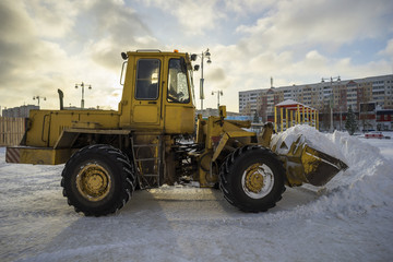 Tractor shovel snow in a pile on the street.