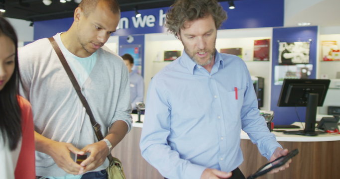 Helpful salesman serving customers in consumer electronics store showroom
