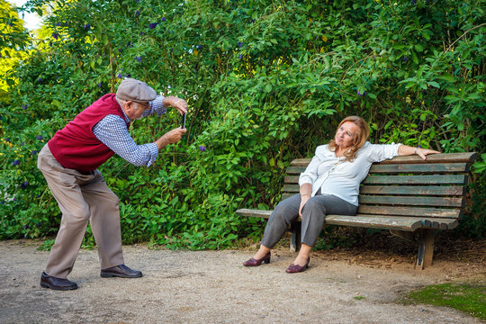 Senior couple in love taking photos in a park. They are 75 years old