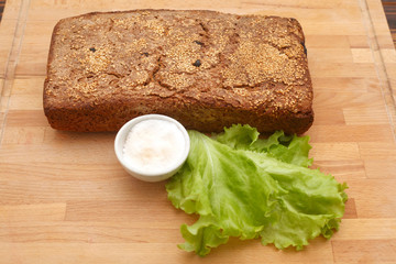 Ржаной домашний хлеб рядом с солью в солонке и листом салата на деревянной доске