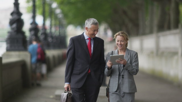 Businesspeople walking, talking and looking at data on tablet and smiling