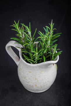 Sprigs of fresh rosemary in a jug on black background