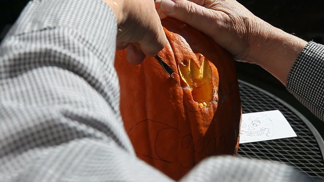 using carving tools to cut out features of a jack o' lantern
