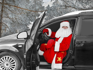 Праздник Новый Год. Современный Дед Мороз - водитель,  сидит за рулем в машине с  мешком  подарков. В заснеженном лесу