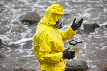 scientist in mask and protective uniform examining  little fishes on hand in glove 