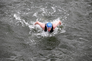 iron man - dynamic and fit swimmer in cap and wetsuit breathing  performing butterfly stroke in dark sea water
