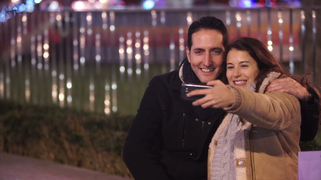 Happy romantic couple pose to take a selfie at Christmas fair