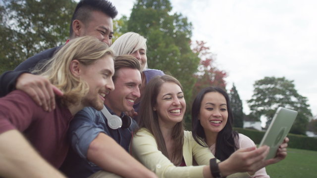  Happy group of friends in natural setting, pose for photo with computer tablet