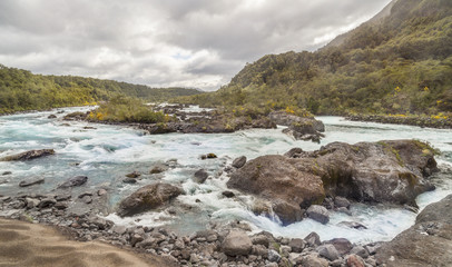 Fototapeta na wymiar Mountain fast flowing river stream of water in the rocks with cloudy sky