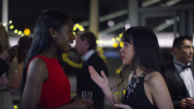  Attractive female friends at sophisticated party embrace and chat together