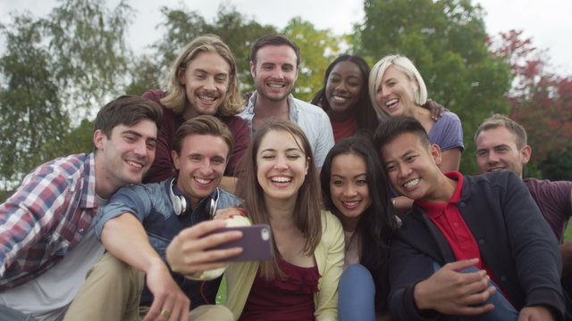 Happy group of friends in natural setting, pose for photo with mobile phone