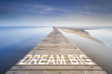A Long jetty at morning over a ocean to the horizon. On the jetty is written the word dream big....
