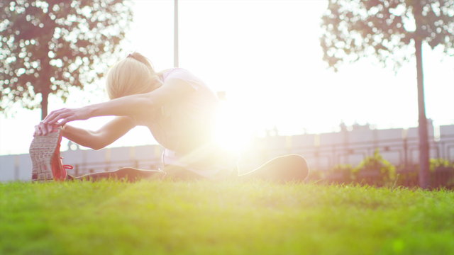  Woman with headphones doing stretches to prepare for her workout in the park