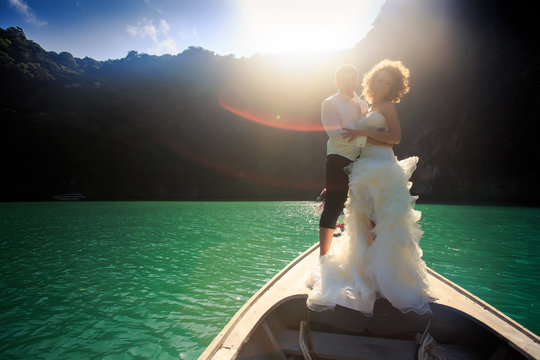 backlight groom blonde bride in fluffy on nose of longtail boat