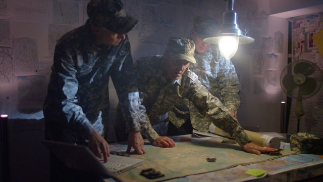  Military officers in army bunker, looking at map & discussing battle strategy