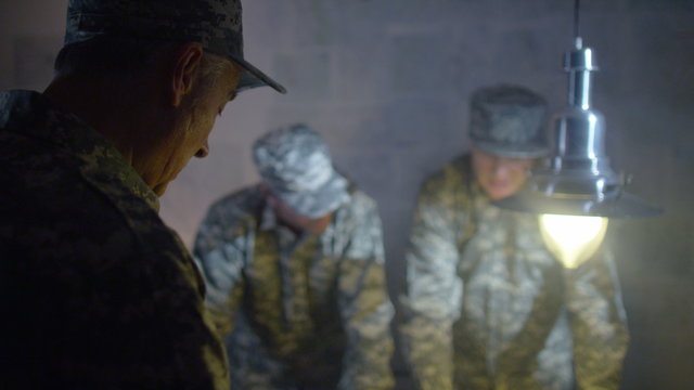  Military officers in army bunker, looking at map & discussing battle strategy