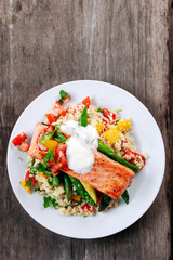 Pan fried Salmon with tender asparagus, courgette served on couscous mixed with sweet tomato, yellow pepper, with greek yogurt on old wooden table.