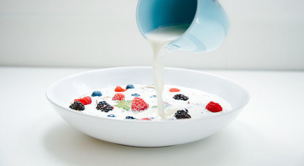 Milk spoil from blue cup to muesli in white plate