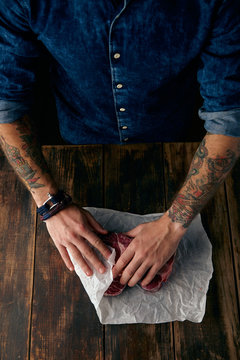 Tattooed hands pack steaks in white craft paper